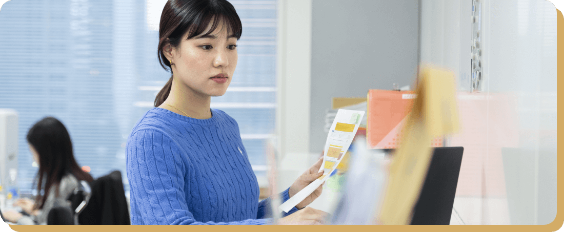 オフィスで女性社員が書類を確認している様子。自動車船の航路について理解を深め、将来的に通関士の資格取得を目指す目標を語る